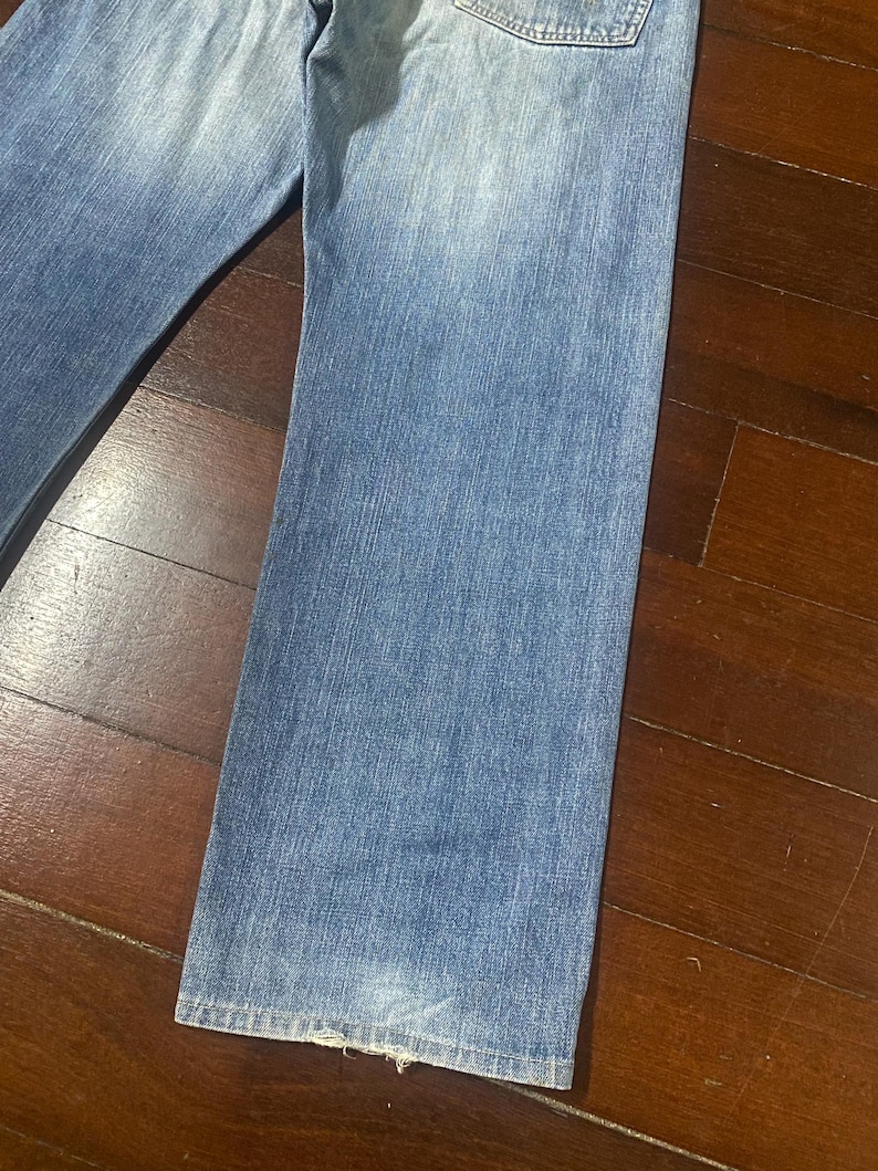 May include: Light blue denim jeans with a faded wash. The jeans have a classic five-pocket design and a straight leg cut. The fabric shows signs of wear and tear, adding to the vintage aesthetic. The jeans are a versatile wardrobe staple.