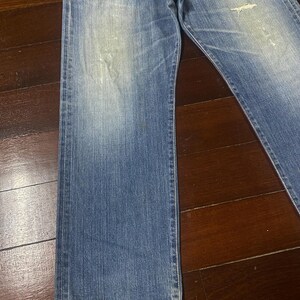 May include: Faded blue denim jeans with a classic straight leg cut. The jeans show signs of wear with distressed areas and light fading throughout. The denim has a medium weight and a traditional five-pocket design.