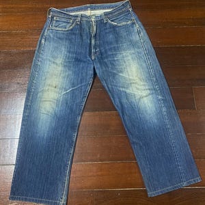 Può includere: Jeans in denim blu sbiadito con un classico design a cinque tasche. I jeans hanno un taglio dritto e mostrano segni di usura, con macchie più chiare sul davanti. Il denim ha un aspetto vintage.