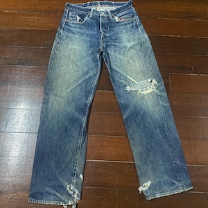 May include: Faded blue denim jeans with distressed details, including rips at the knees and frayed hems. The jeans have a button fly and classic five-pocket design. The denim has a worn, vintage look.
