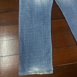 May include: Faded blue denim jeans with a straight leg cut. The jeans show wear and tear at the hem, with a slightly distressed appearance. The denim has a classic, washed look.