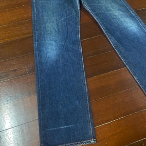 May include: Dark blue denim jeans with a classic straight-leg fit. The jeans have a faded wash and visible stitching along the seams. The denim appears to be a medium weight, suitable for everyday wear.