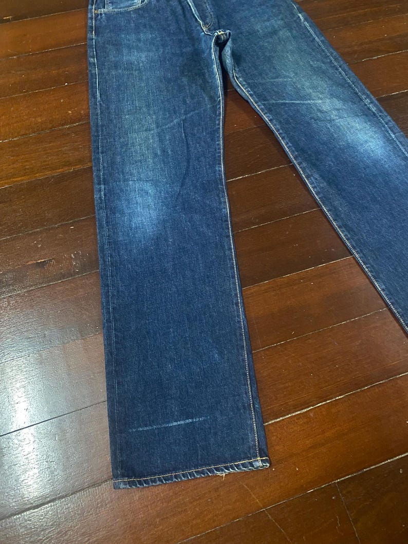 May include: Dark blue denim jeans with a classic straight-leg fit. The jeans have a faded wash and visible stitching along the seams. The denim appears to be a medium weight, suitable for everyday wear.