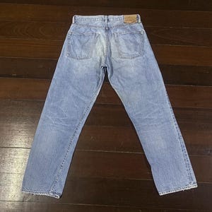 May include: Light blue denim jeans with a classic five-pocket design. The jeans have a faded wash and a leather patch on the back waistband. The straight-leg cut offers a timeless style.