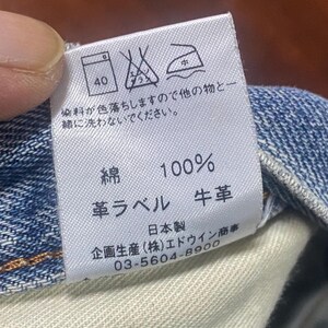 May include: A close-up of a white clothing label with Japanese text and care symbols. The label states the material is 100% cotton and has a leather label. A phone number is also visible.
