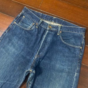 May include: A pair of classic blue denim jeans. The jeans have a button fly, five-pocket design, and a straight leg cut. The denim has a medium wash with subtle fading and wear marks.