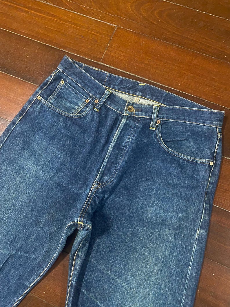 May include: A pair of classic blue denim jeans. The jeans have a button fly, five-pocket design, and a straight leg cut. The denim has a medium wash with subtle fading and wear marks.