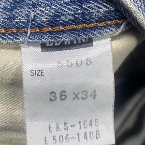 May include: Close-up of a white label from blue denim jeans. The label shows the size as 36 x 34 inches (91.4 x 86.4 cm), along with the number 5505 and other codes. The jeans are made of denim.