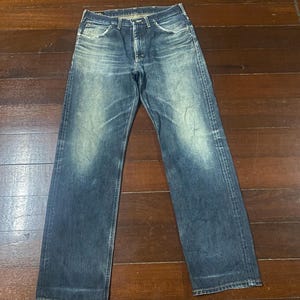 May include: A pair of blue denim jeans with a faded wash. The jeans have a classic five-pocket design and a straight leg fit. The denim has a worn appearance, with lighter areas on the thighs and knees.
