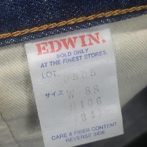 May include: Close-up of a denim garment tag with the brand name "EDWIN" in red. The tag includes text indicating the product is sold only at the finest stores, along with size and care information.
