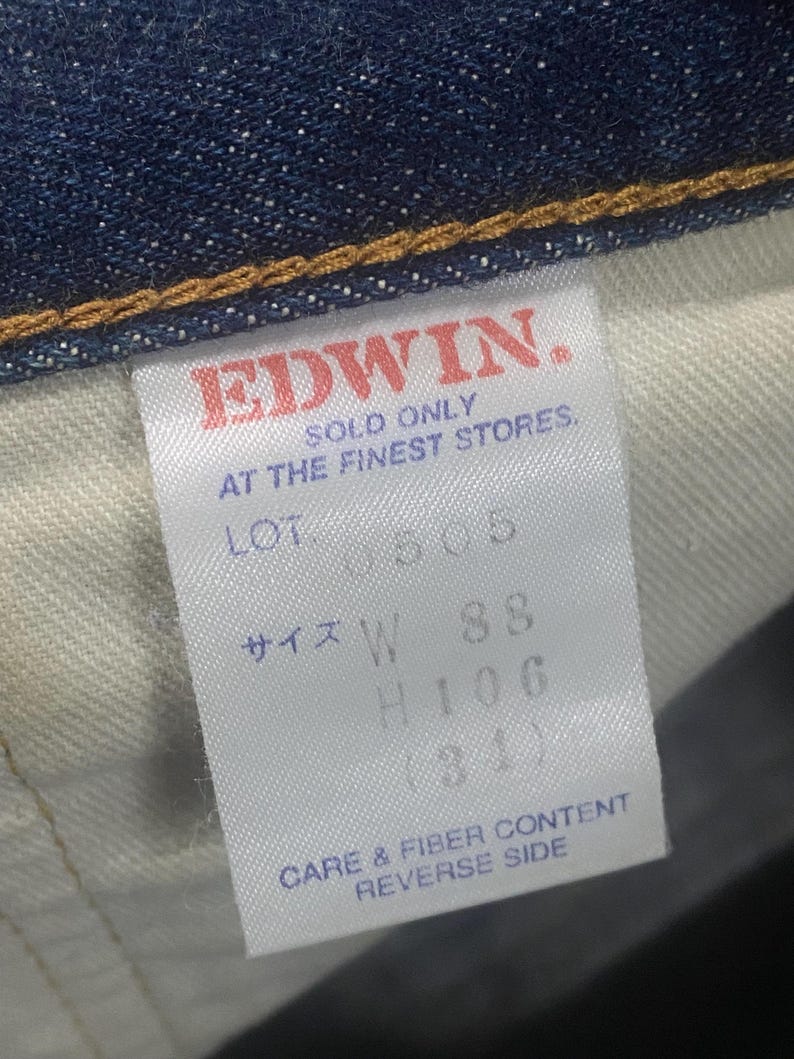 May include: Close-up of a denim garment tag with the brand name "EDWIN" in red. The tag includes text indicating the product is sold only at the finest stores, along with size and care information.
