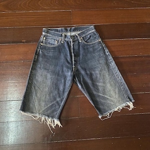 May include: Dark blue denim shorts with a button fly and frayed edges. The shorts have a classic five-pocket design and show signs of wear, with faded areas and distressed details. The shorts are approximately 18 inches long.
