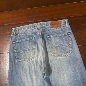 May include: Light blue denim jeans with a classic five-pocket design. The back of the jeans features two pockets and a brown leather patch with the brand name "EDWIN". The jeans are made of a durable denim fabric.