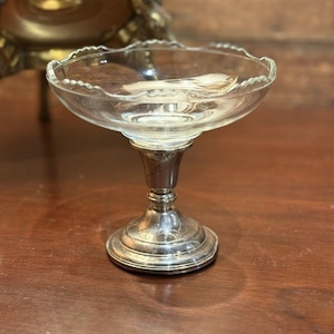 May include: A clear glass pedestal bowl with a silver base. The bowl has a scalloped edge and the base has a fluted design.