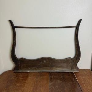 May include: A vintage wooden display rack with a dark brown finish. The rack features a curved top and sides, with a horizontal bar for hanging items. The base has a decorative, wavy design.
