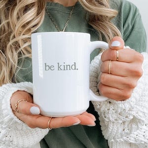 May include: White ceramic mug with the text "be kind." in gray lettering. The mug has a large handle and a simple, clean design. A perfect gift for anyone who appreciates a positive message.