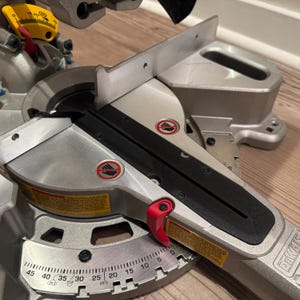 May include: A silver and black miter saw with a red lever. The saw has a protractor with markings from 0 to 45 degrees. The saw is made by the brand Dewalt.