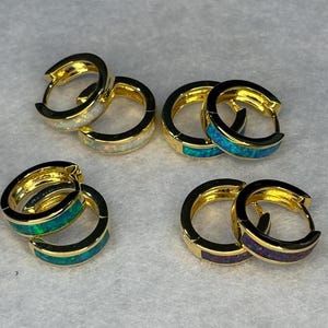May include: Four pairs of gold hoop earrings with opal inlay. The earrings are in different colors, including white, blue, and purple.