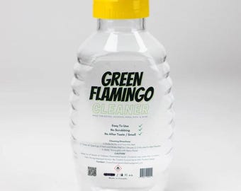May include: A clear plastic bottle with a yellow lid labeled "Green Flamingo Cleaner" made for bongs, hookahs, pipes, rigs, and more. The bottle has a green checkmark next to "Easy To Use", "No Scrubbing", and "No After Taste / Smell".