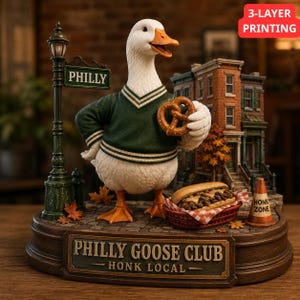Op de afbeelding: Een beeldje van een witte gans in een groene trui met witte strepen, die een bruine krakeling vasthoudt. De basis bevat een lantaarnpaal met een PHILLY-bord, een bakstenen gebouw, een cheesesteak in een mandje en een bord PHILLY GOOSE CLUB HONK LOCAL.