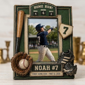 Op de afbeelding: Een rechthoekige fotolijst met honkbalthema in donkergroen met een scorebord bovenaan met de tekst HOME RUN! HOME 4, INNING 6, GUEST 2. Het bevat een honkbalknuppel, een handschoen met bal, een honkplaat met nummer 7 en schoenen. Tekst: NOAH #7 FIRST HOME RUN • MAY 12, 2026.