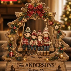 May include: A wooden Christmas tree-shaped ornament featuring a swing with four figures wearing winter hats and sweaters. The base displays the text "The ANDERSONS" and "Christmas 2026," with names "David," "Ethan," "Sophie," and "Emma" below the swing.