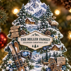 May include: A tree-shaped Christmas ornament featuring a snowy mountain landscape, a log cabin, an elk, skis, snowshoes, and goggles. The center plaque reads THE MILLER FAMILY COLORADO CHRISTMAS 2026, with signs saying EXPLORE, SKI, HIKE, BELONG, and HIGHER TOGETHER.