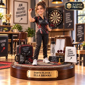 May include: A figurine of a darts player named Ella Brooks standing on a circular wooden base. The figure wears a black polo with red and white accents, black trousers, and white trainers. Accessories include a dart case, mug, water bottle, and towel, all featuring motivational text about darts.