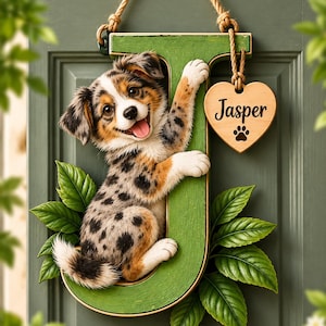 Könnte beinhalten: Ein grüner Wandbehang in Form des Buchstabens J mit einem gefleckten Australian Shepherd Welpen, der an dem Buchstaben hochklettert. Ein kleines hölzernes Herzschild hängt oben daran, beschriftet mit dem Namen Jasper und einer schwarzen Pfote.