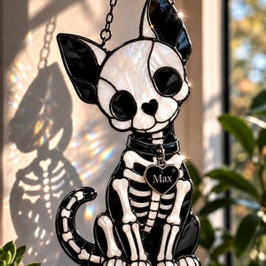 May include: A stained glass suncatcher shaped like a sitting cat skeleton with black and white glass pieces. The cat features a black collar with a heart-shaped tag engraved with the name Max, and it hangs from a black metal chain.