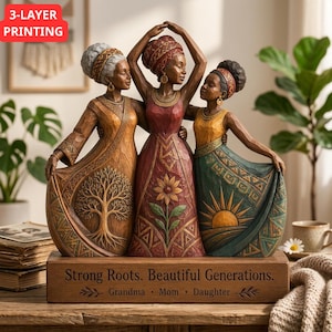 May include: A resin sculpture of three figures representing a grandmother, mother, and daughter standing together. The base is inscribed with the text "Strong Roots. Beautiful Generations. Grandma • Mom • Daughter" and features a tree, sunflower, and sun.