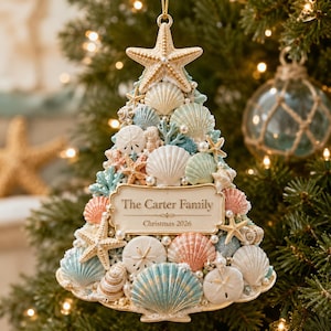 May include: A triangular Christmas tree ornament crafted from various seashells, starfish, and sand dollars in shades of white, blue, and peach. A central rectangular plaque features the text The Carter Family and Christmas 2026.