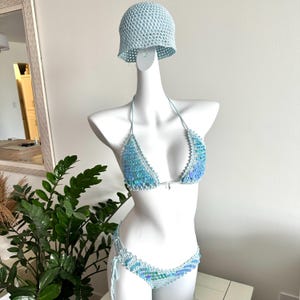 May include: A light blue crochet bikini set with a matching bucket hat. The bikini top and bottom are embellished with iridescent sequins. The set is displayed on a white mannequin.