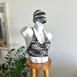 May include: A black and white crocheted halter top featuring a textured pattern and a matching crocheted beanie hat. The halter top has thin black straps and a central button detail, while the beanie displays a consistent black and white design.