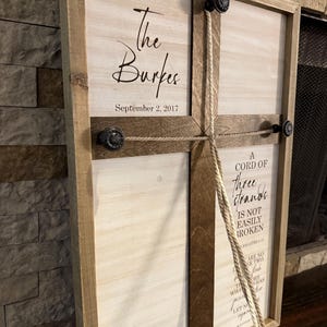 May include: Wooden framed sign with the text "The Burkes September 2, 2017" in elegant script. The sign also features the text "A cord of three strands is not easily broken." Decorative knobs and rope add to the rustic charm.