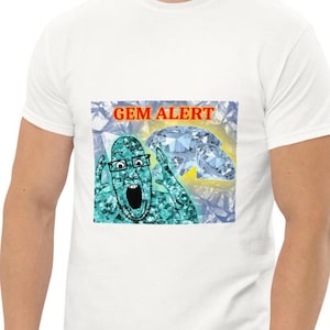 Puede incluir: Camiseta blanca con un gráfico de dibujos animados con el texto "GEM ALERT". El gráfico representa una cara sorprendida con gafas y un gran diamante. El fondo es un patrón de diamantes.