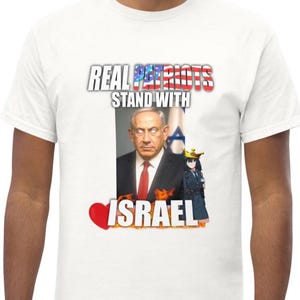 Puede incluir: Camiseta blanca con el texto "REAL PATRIOTS STAND WITH ISRAEL". El gráfico incluye un retrato de un hombre con traje y corbata, y un personaje de estilo anime. El diseño incorpora la bandera israelí.
