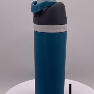 Peut inclure: Une bouteille d'eau bleu sarcelle avec un couvercle gris et blanc. Le couvercle a un anneau en silicone bleu.