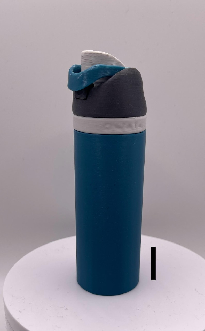 Peut inclure: Une bouteille d'eau bleu sarcelle avec un couvercle gris et blanc. Le couvercle a un anneau en silicone bleu.