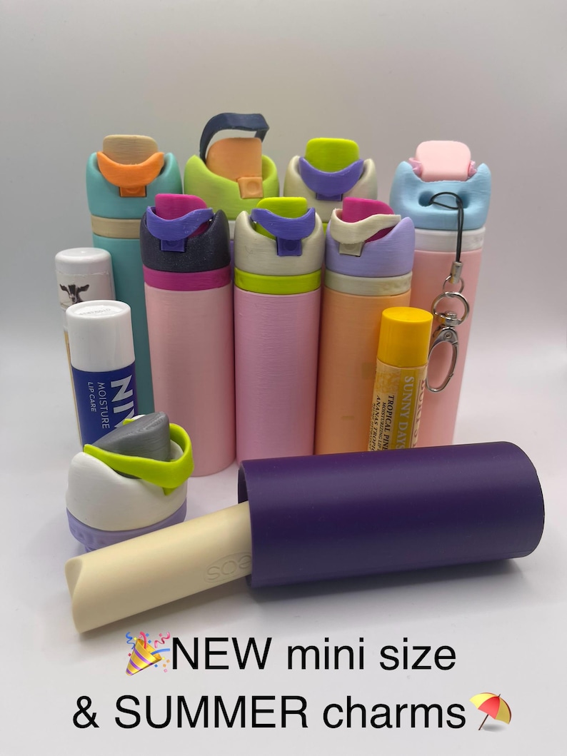 Peut inclure: Une collection de mini bouteilles d'eau color&eacute;es avec des couvercles et des breloques de diff&eacute;rentes couleurs. Les bouteilles sont dispos&eacute;es en demi-cercle avec un tube violet et un baume &agrave; l&egrave;vres au centre. Le texte "NEW mini size & SUMMER charms" est en bas de l'image.