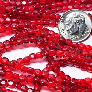May include: A strand of red glass beads, each bead is square shaped with rounded edges. The beads are approximately the size of a US dime.
