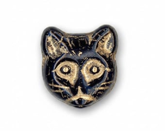 May include: A small, flat, cat-shaped bead featuring a glossy black finish with gold-colored detailing. The design highlights the cat's facial features, including pointed ears, wide eyes, a small nose, and whiskers, all outlined in a metallic gold tone.