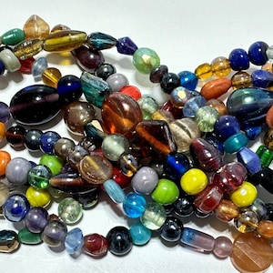 May include: A collection of colorful glass beads in various shapes and sizes, including round, oval, and teardrop. The beads are arranged in a loose pile, showcasing a wide range of colors, such as blue, green, red, orange, and yellow.