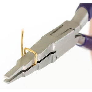 May include: A pair of metal pliers with dark purple handles gripping a bent piece of gold-colored wire. The pliers feature a flat, tapered jaw design, and the gold wire is shaped into a small, rectangular loop with one end extending upward.