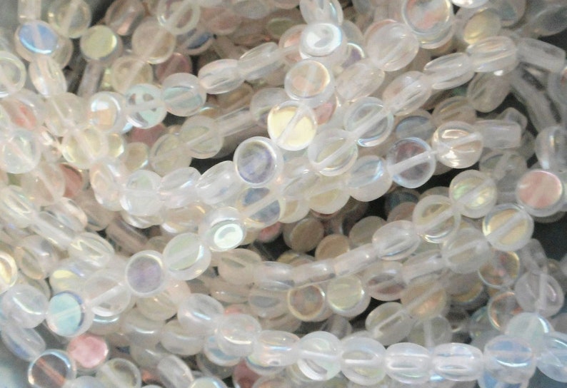 May include: A strand of iridescent white glass beads. The beads are round and flat, with a slightly oval shape. They have a subtle shimmer and are perfect for jewelry making.