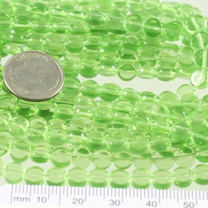 May include: A strand of light green glass beads, approximately 6mm in diameter. The beads are round and have a smooth, polished finish. The beads are strung on a clear thread and are arranged in a loose, flowing pattern.