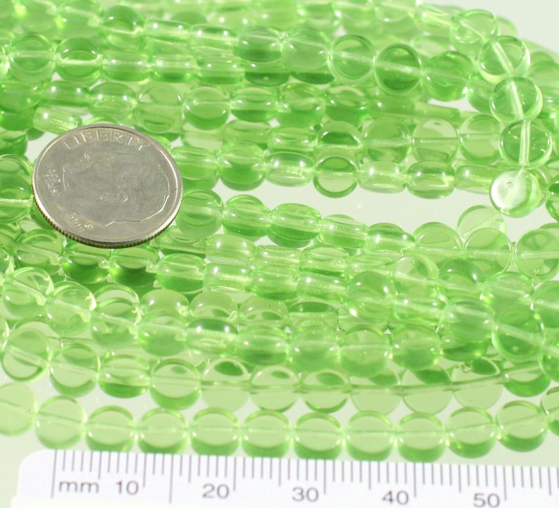 May include: A strand of light green glass beads, approximately 6mm in diameter. The beads are round and have a smooth, polished finish. The beads are strung on a clear thread and are arranged in a loose, flowing pattern.