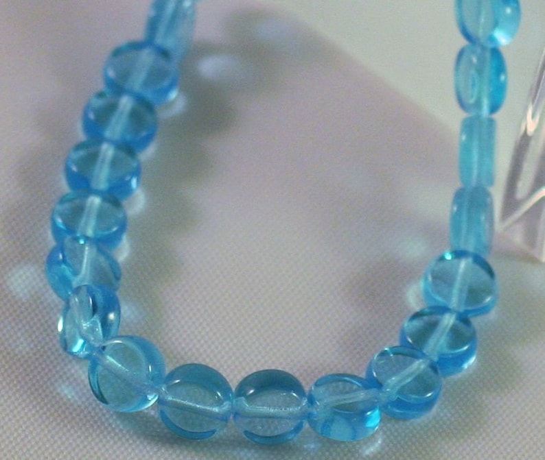 May include: A strand of light blue glass beads, each bead is round and slightly translucent.