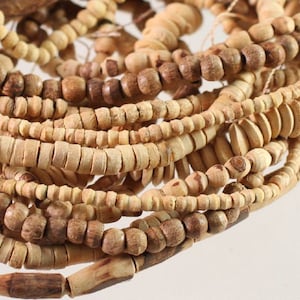May include: A close-up of a pile of wooden beads in various shades of brown and beige. The beads are of different shapes and sizes, some are round, some are oval, and some are cylindrical.