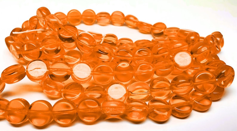 May include: A strand of round, translucent orange glass beads. The beads are approximately 10mm in diameter and have a slightly flattened shape.